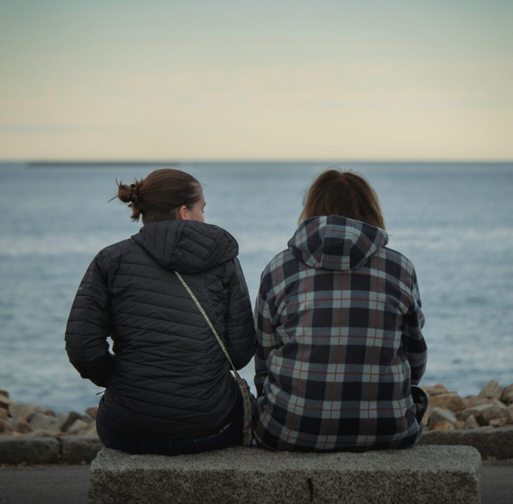Two people sitting on a bench looking out over water